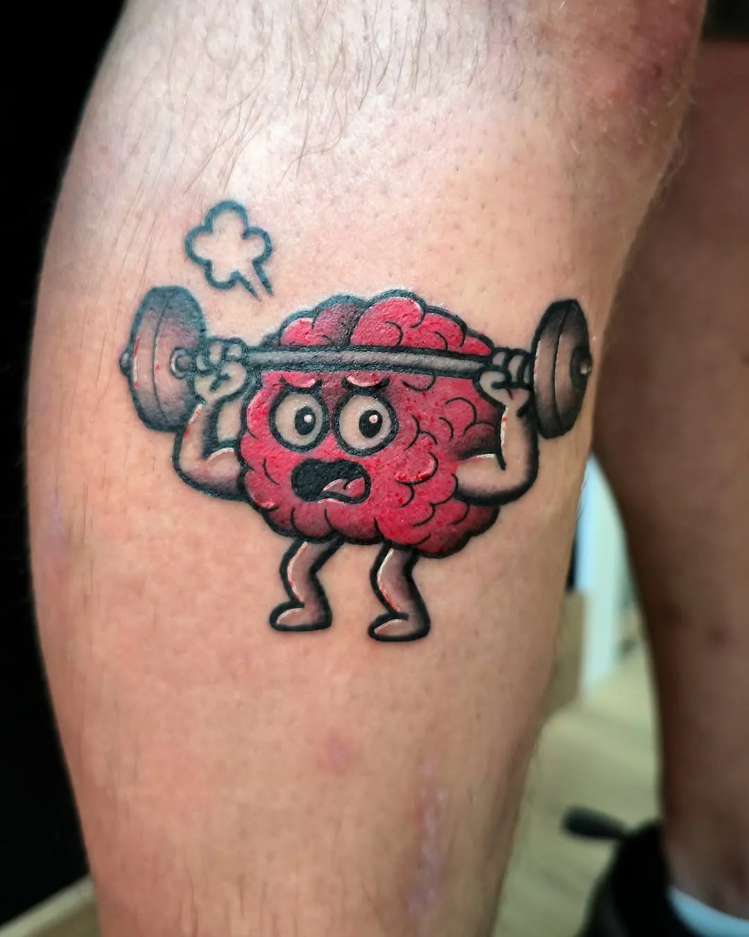 Tatuaje cartoon a color de un cerebro musculado levantando pesas