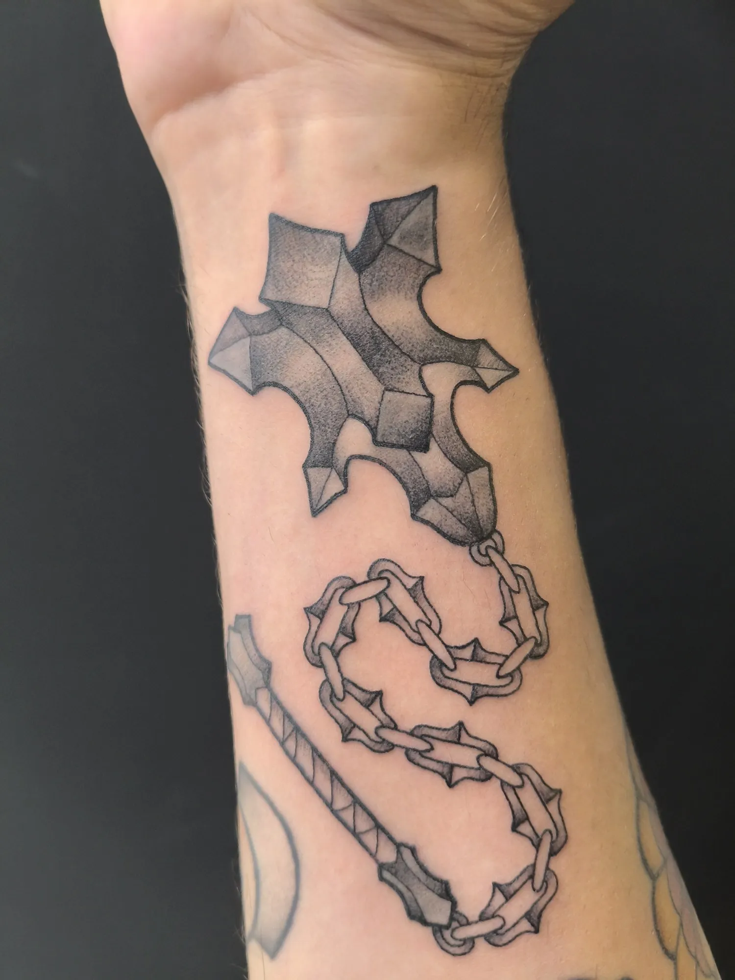 Tatuaje dotwork de cruz con cadena en el antebrazo
