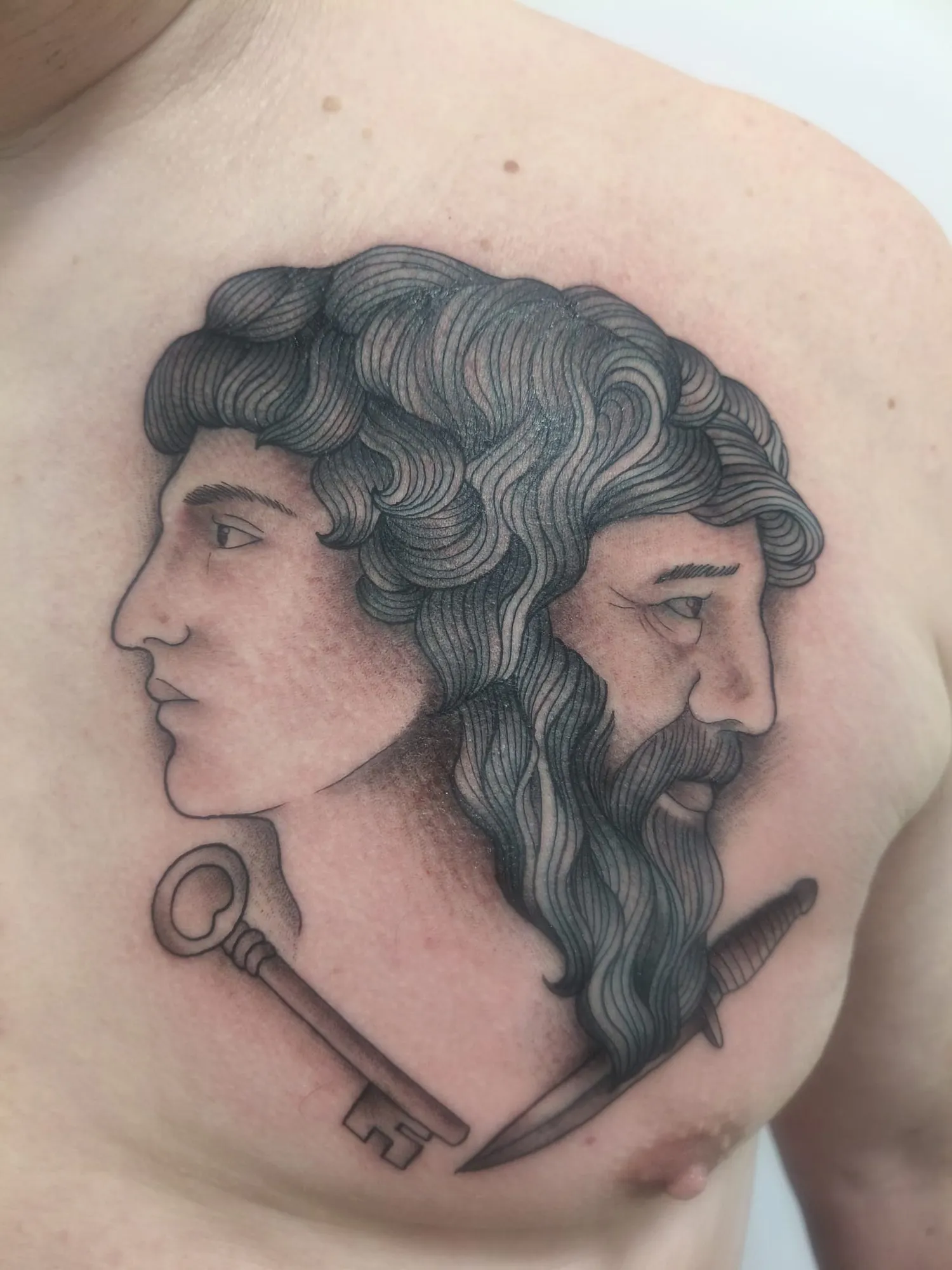 Tatuaje blackwork de Jano de dos caras con llave y daga en el pecho