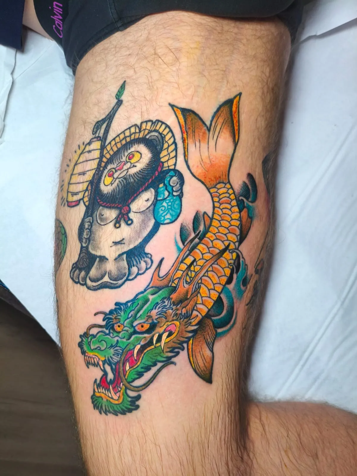 Tatuaje japonés a color de pez koi, dragón y shisa en el muslo
