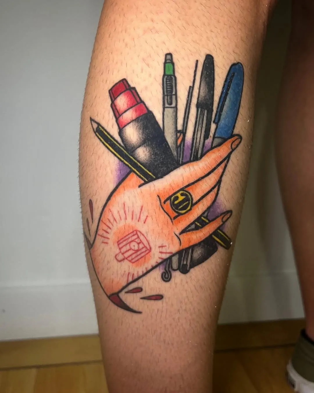 Tatuaje tradicional a color de una mano sujetando lápices y rotuladores