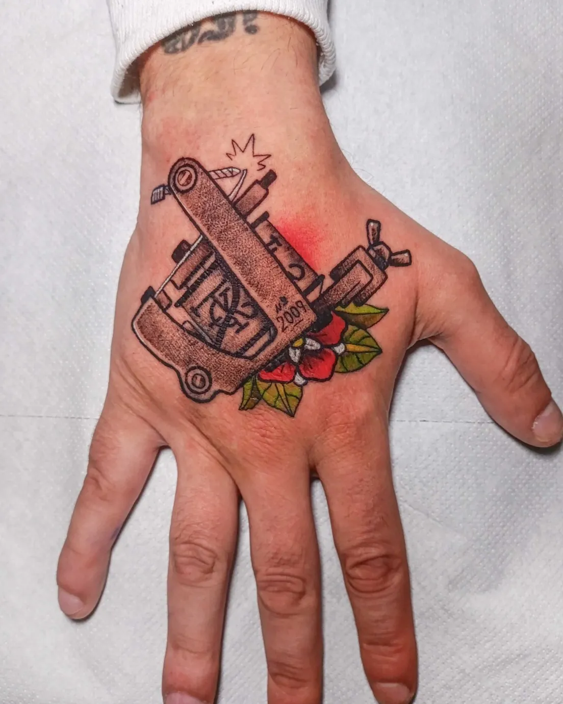 Tatuaje tradicional de máquina de tatuar con flor en la mano
