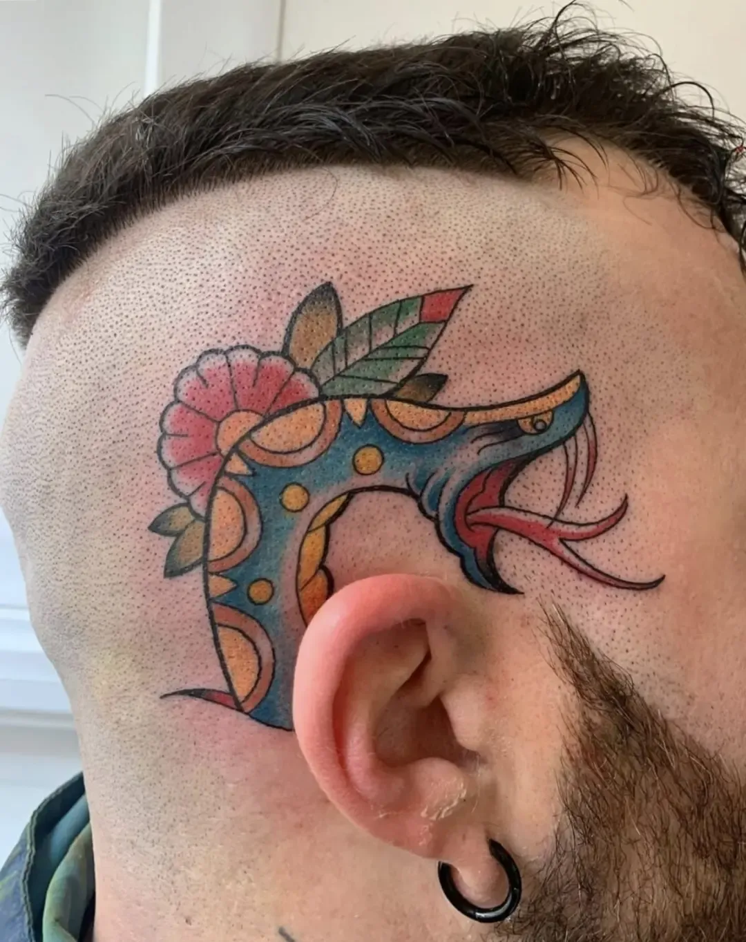 Tatuaje tradicional a color de cabeza de serpiente con flores en la cabeza