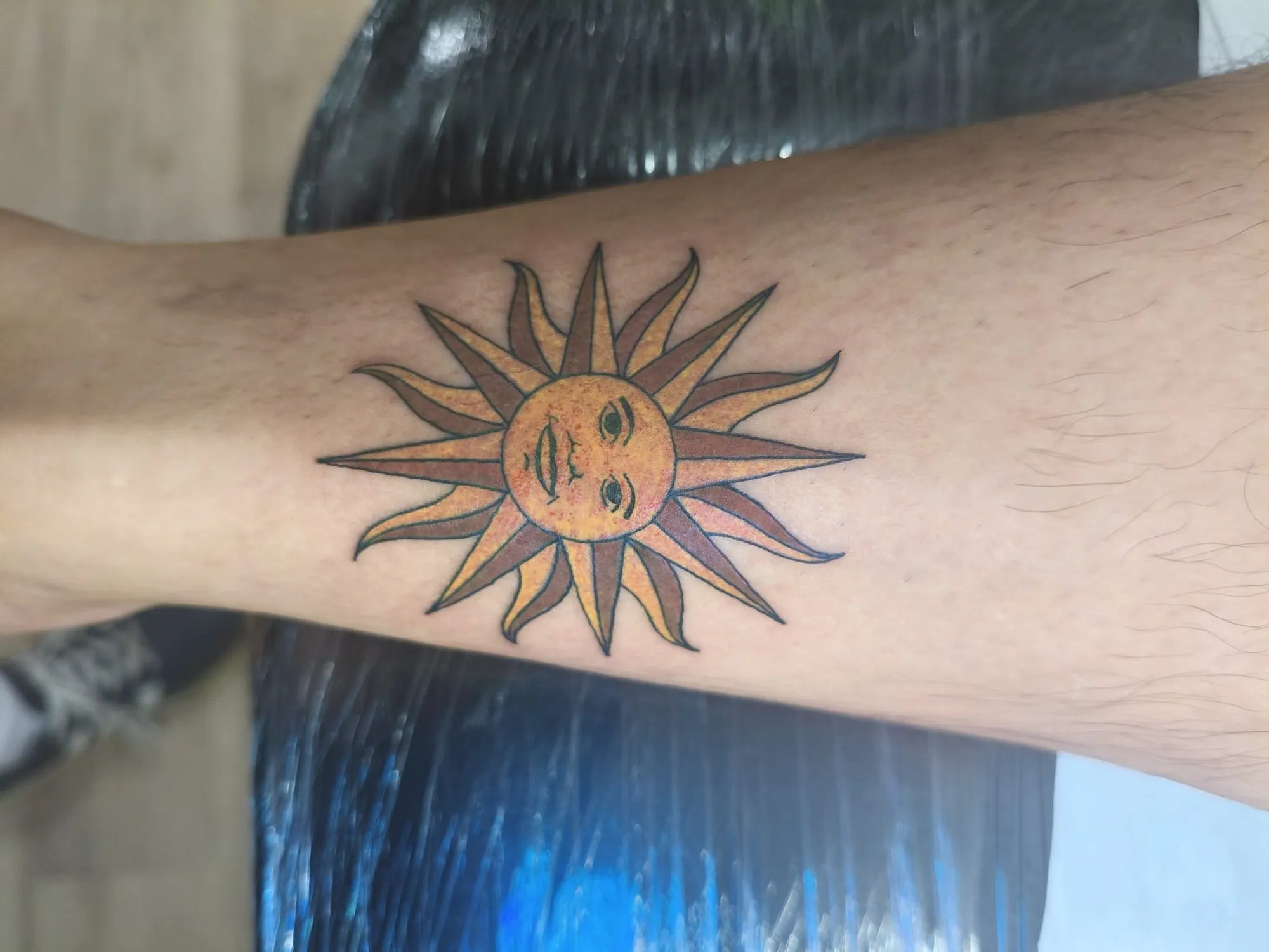 Tatuaje tradicional de sol a color en el antebrazo